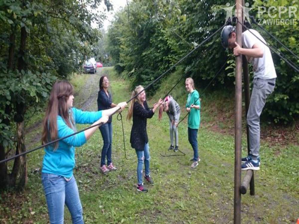 Zdjęcie: Dziewczynki naciągają liny umocowane do konstrukcji z belek w kształcie litery A, na której stoi chłopiec w kasku